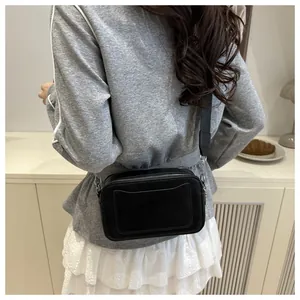 Close-up of a black leather camera bag with wide fabric strap on a model's shoulder