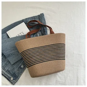 Dettaglio borsa tote in paglia intrecciata con strisce nere e manici marroni su denim