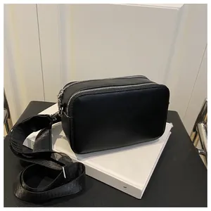 Detail of dual silver zippers and wide fabric strap on a black leather camera crossbody bag