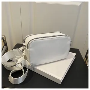 Detail view of the white crossbody camera bag with double metal zippers and wide strap