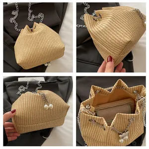 Detail view of woven straw bucket bag with silver chain strap and pearl charm accent