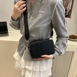 Chic black camera crossbody bag with wide shoulder strap worn by a model in lifestyle setting