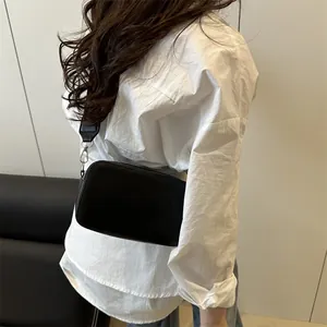 Modern minimalist black leather camera bag with wide strap worn as crossbody