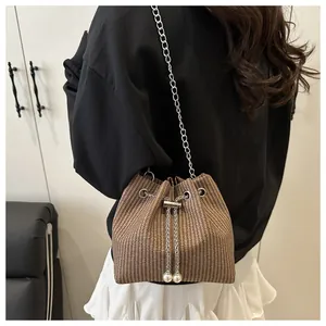 Detail of woven brown bucket bag with pearl drawstring and silver chain strap on model