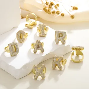 Vergoldete Alphabet-Ringe mit Zirkonia-Steinen auf einem weißen Steinsockel