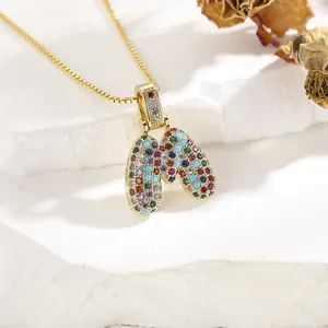 Macro detail of gold letter M pendant with colorful zircons on a white gypsum pedestal