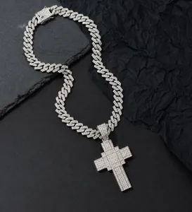 Gros plan du pendentif croix serti et chaîne cubaine argentée sur fond en pierre noire