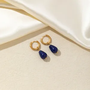 Dettaglio di orecchini a cerchio dorati con pietre blu a goccia su seta