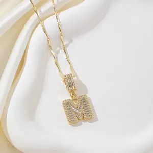 Vue détaillée du pendentif lettre M doré serti de zircons sur un tissu en soie