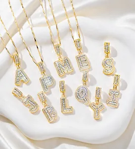 Détail de pendentifs alphabet dorés avec zircons posés sur un tissu en soie blanc