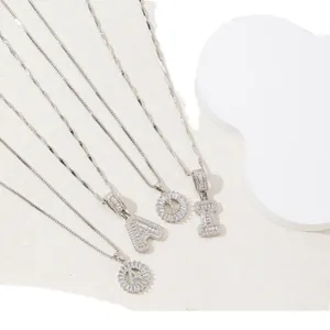 Collane con ciondoli a lettera in argento con pavé di zirconi su base espositiva bianca elegante
