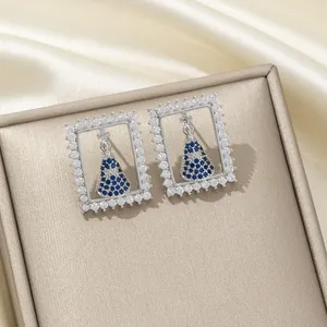 Détail de boucles d'oreilles argentées avec zircons et centre bleu de la Vierge Marie