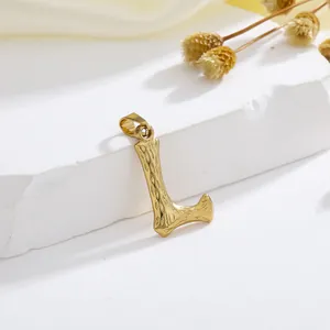 Detailopname van gouden letter L hanger met schorsstructuur op een stenen voet
