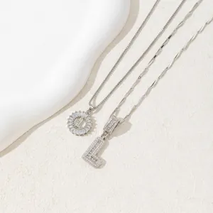 Macro detail of silver tone initial L pendants with cubic zirconia on textured background