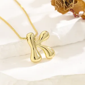 Detailed view of polished gold letter K pendant on a box chain over white stone