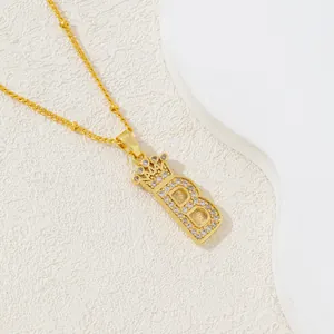 Collier doré avec pendentif lettre B et couronne orné de zircons sur fond blanc