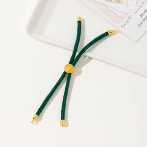 Detail of dark green woven bracelet with gold Tree of Life charm on a white tray
