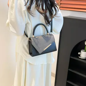Fashionable black and grey crossbody bag with gold trim worn by a model in interior