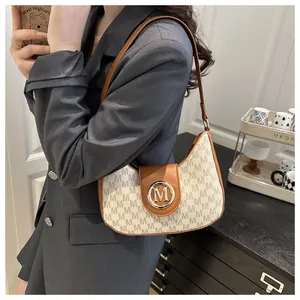 Détail du sac porté épaule vintage avec boucle dorée en M et finitions en cuir marron