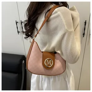 Détail du sac demi-lune rose avec bandoulière marron et fermoir métallique doré en M