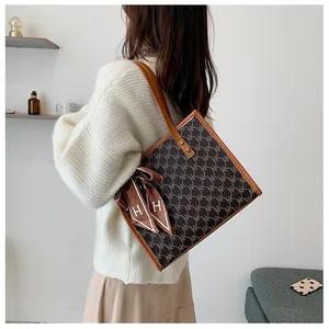 Detail of printed tote bag with brown leather trim and silk scarf accessory on strap