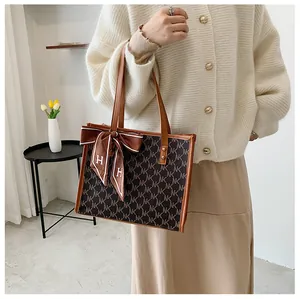 Detailed shot of retro tote bag with monogram pattern and silk scarf on leather handle