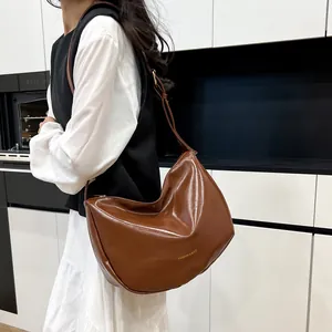 Brown faux leather crescent underarm bag with adjustable strap shown on model in kitchen
