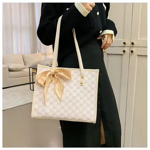 Detail of beige tote bag with brown monogram pattern and champagne silk scarf on handle
