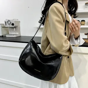 Fashionable black faux leather underarm bag with gold lettering shown in a cafe setting