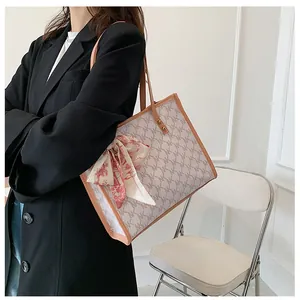Beige tote bag with NK monogram pattern and red floral scarf on a black blazer