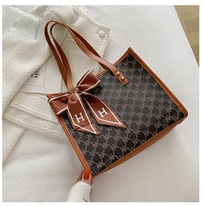 Close-up of brown tote bag with NK pattern, metallic rivets and decorative H logo ribbon