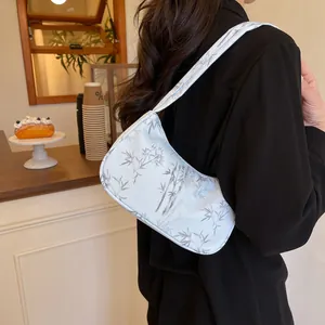 Chic white underarm bag with bamboo pattern shown on shoulder in a cafe setting