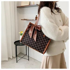 Brown monogram tote bag with leather handles and decorative silk scarf detail