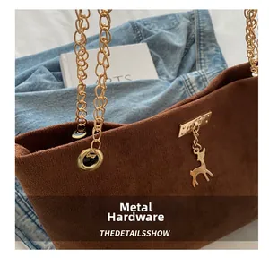 Detail of metal chain link and gold deer charm on a brown suede tote bag