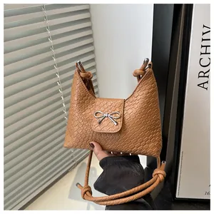 Detail of camel woven texture handbag featuring a silver metal bow accent and knotted strap