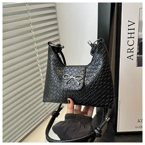 Detail of black woven tote bag featuring a silver metal bow accent and knotted rope straps