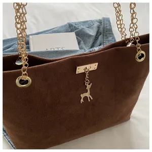 Detail of dark brown matte tote bag with gold chain straps and a small deer charm