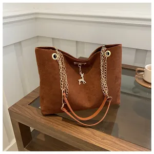 Detail of brown suede tote bag with golden chain straps and deer charm on glass table