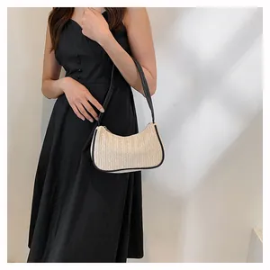 Detail of hand-woven straw hobo bag with black trim and strap worn with black dress