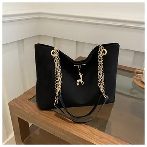 Close-up of black matte tote bag featuring gold chain strap and a deer charm pendant
