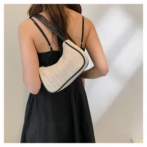 Detail of woven hobo shoulder bag with black leather trim worn by a model in black dress