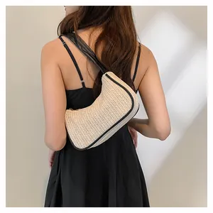 Model wearing a hand-woven straw hobo bag with black leather trim and shoulder strap
