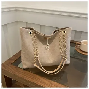 Detail of khaki frosted tote bag with metal chain strap and deer charm on wooden table