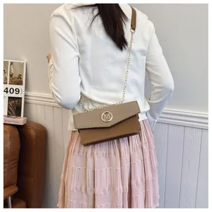 Detail of brown square crossbody bag with woven texture, M-buckle, and gold chain strap