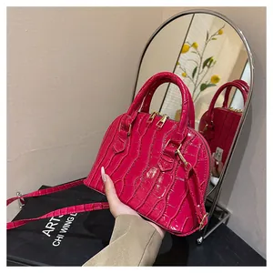 Detail of rose pink crocodile embossed dome bag with gold zippers and detachable strap