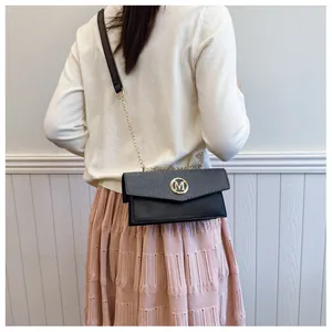 Rear view of model wearing black square bag with gold M logo and chain strap