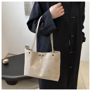 Detail of beige suede tote bag with golden chain strap and deer charm on black coat