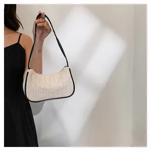 Detail of woven straw hobo bag with black leather trim shown in aesthetic soft lighting