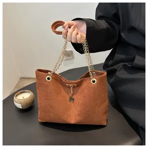 Close-up of brown suede tote bag featuring gold chain handle and deer charm detail