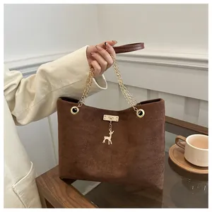 Detail of a brown frosted suede handbag featuring a gold deer charm and chain strap